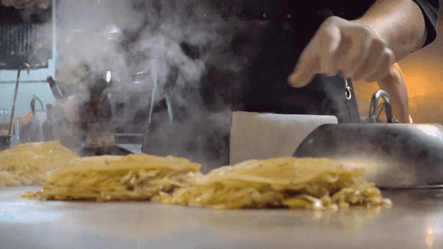 Chef preparing okonomiyaki on a hot griddle