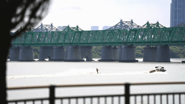 Boat and water skier near a green bridge