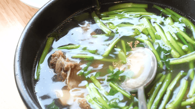 Spoon stirring galbitang broth containing water parsley and beef