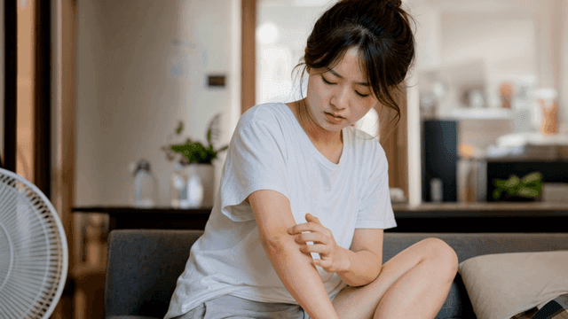 Woman scratching her arm at home