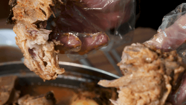 Gamjatang pork backbone meat held and torn by gloved hands