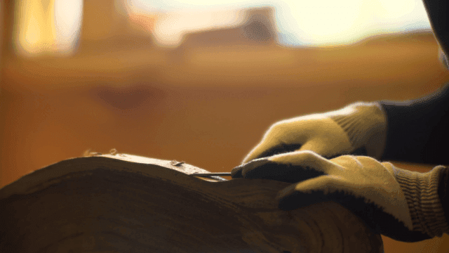 장갑을 낀 손이 실내에서 나무를 조각하는 모습