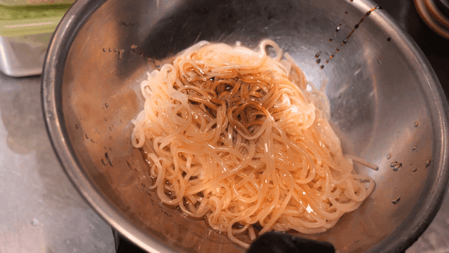 Noodles being seasoned in a metal bowl