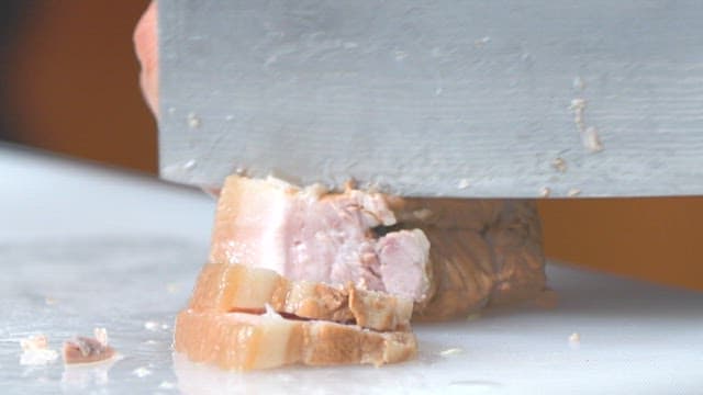 Slicing boiled pork slices on a cutting board with a knife in a kitchen