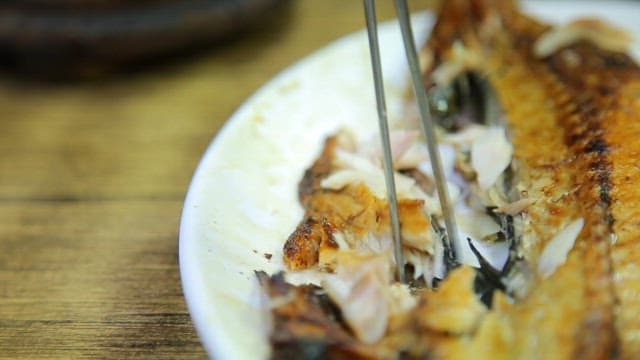 Cutting the glossy, golden grilled mackerel with chopsticks