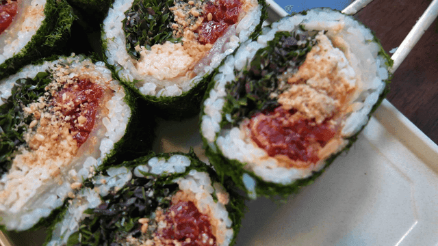 Chopsticks picking up aged kimchi and seaweed roll filled with various ingredients