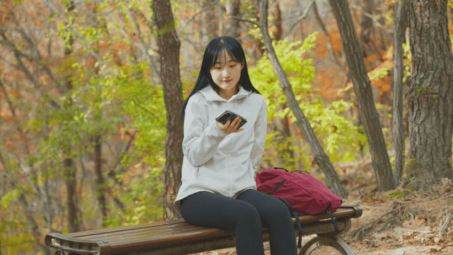 Young woman resting on bench using smartphone in autumn forest