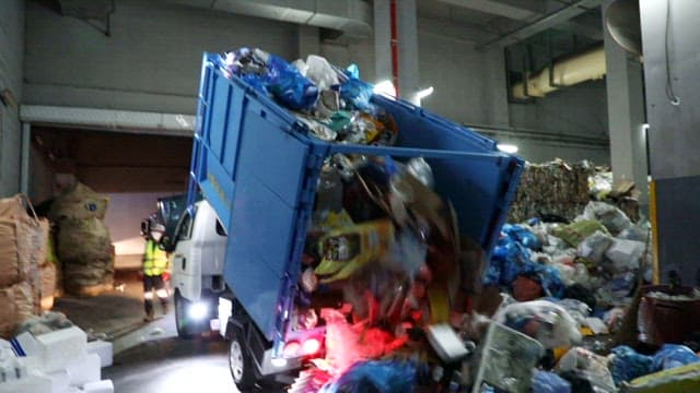 Garbage truck unloading recyclables in an indoor facility at night