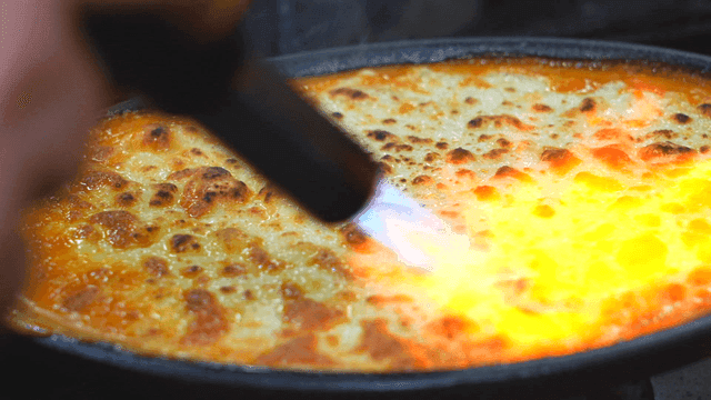 Cheese being torched on a dish