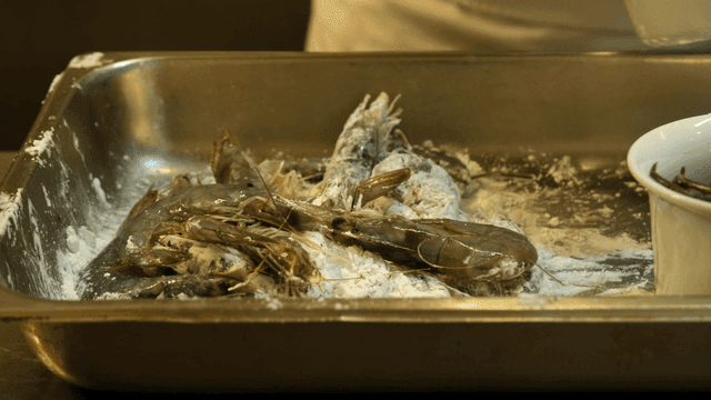 Shrimp being coated with flour in a tray