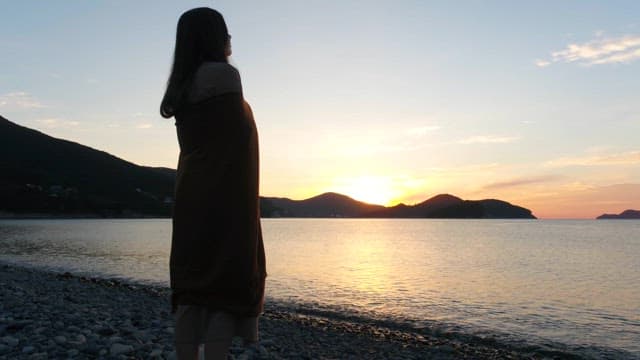 Back of a Woman Watching the Sunset on a Pebble Beach