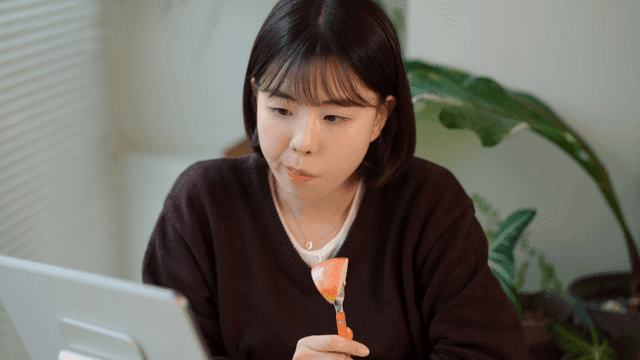 Young woman eating apple while studying on tablet