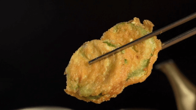 Korean pan-fried battered summer squash held with chopsticks