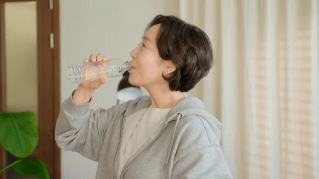 Woman smiling while drinking water indoors