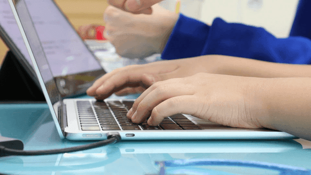 Hands typing on a laptop in a classroom