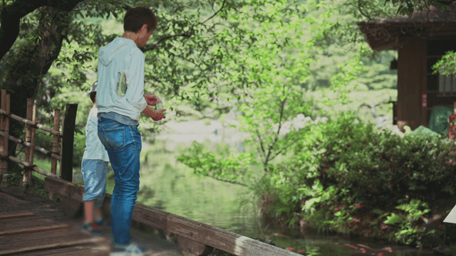 Father and son feeding fish by a pond