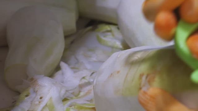 Hands wearing gloves peeling white radishes.