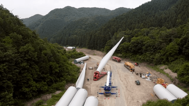 울창한 숲 속 도로에서 풍력 터빈 자재를 운반하는 모습