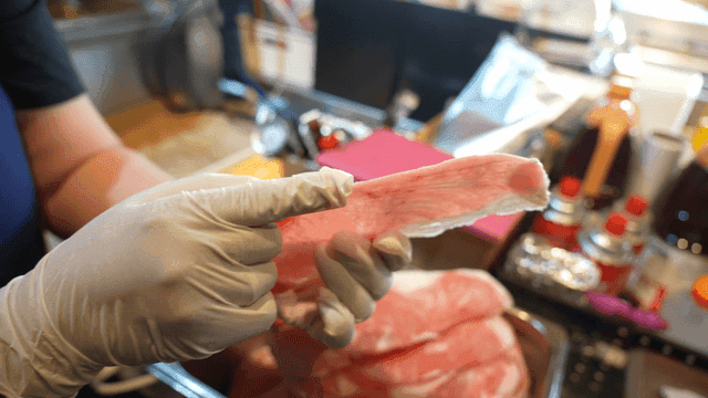 Person who handles frozen raw meat while wearing gloves