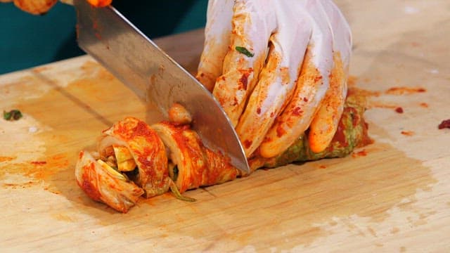 Kimchi being sliced on a wooden board