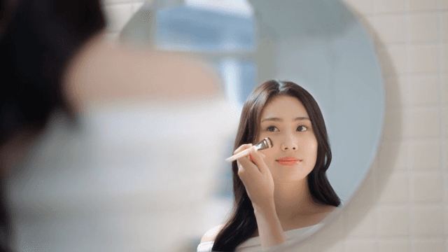 거울 앞에서 브러쉬를 이용해 화장을 하고있는 여성