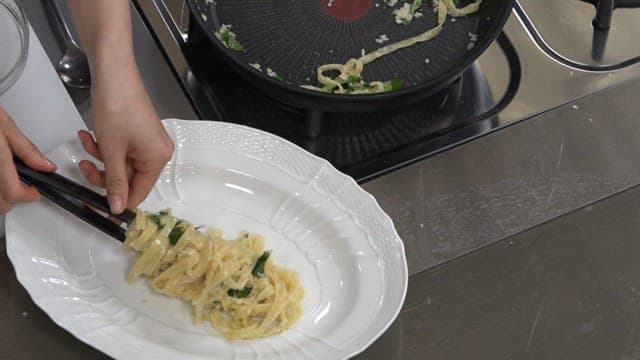 Person serving pasta onto a plate inside a kitchen