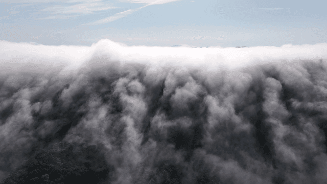 Clouds rolling over a lush green mountain