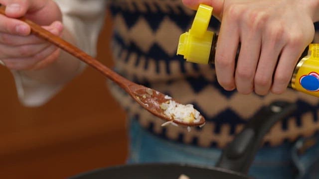 Drizzling sesame oil over egg fried rice in a frying pan