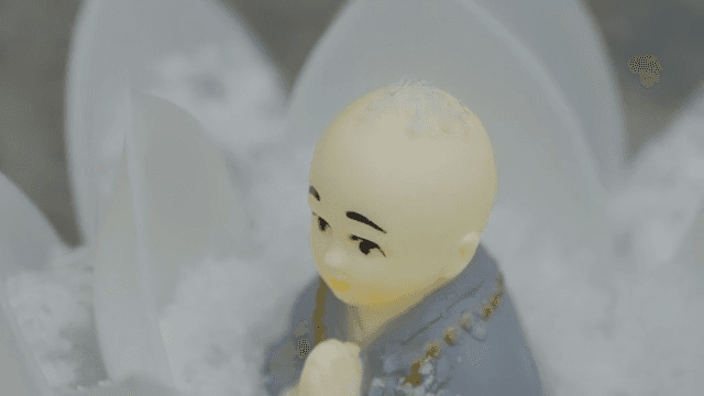 눈에 둘러싸인 작은 승려 조각상