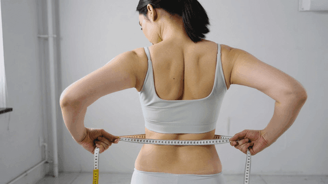 Back view of woman measuring her waist with tape measure