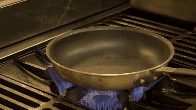 A frying pan heating on a gas stove