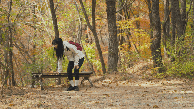 Young woman massaging legs on bench in autumn forest