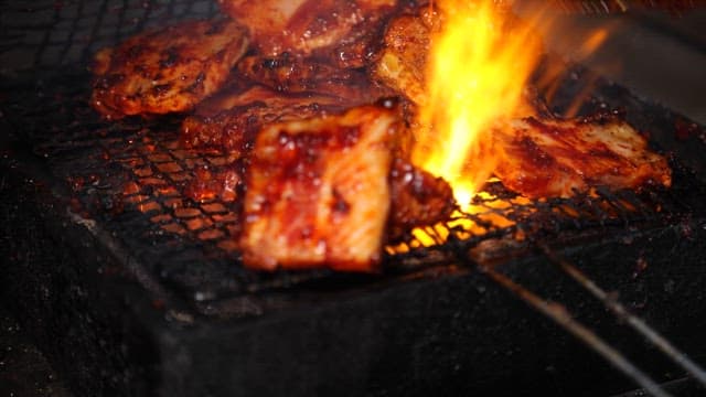 Spicy grilled pork belly sizzling on a grill over blazing charcoal