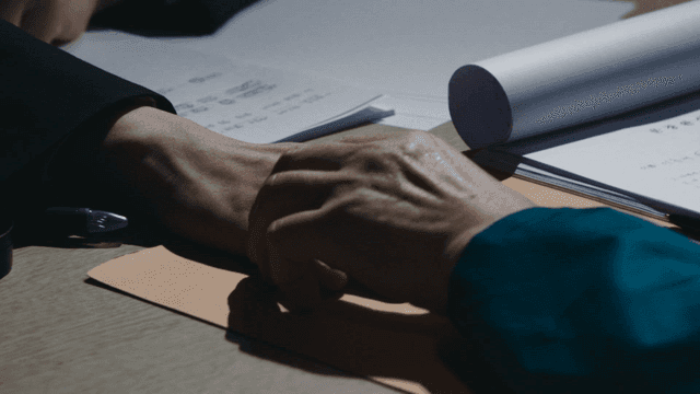 Two people holding hands while discussing documents at table