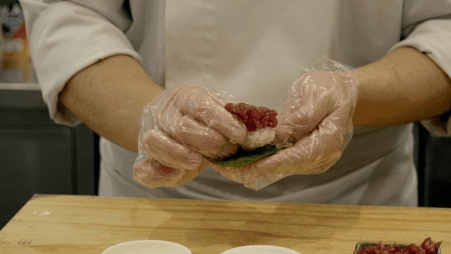 Chef carefully prepares raw fish sushi.