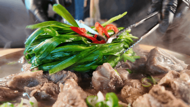 Chives being cut with scissors on top of beef rib hot pot
