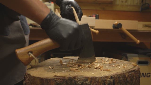 Person carving wood with an axe indoors