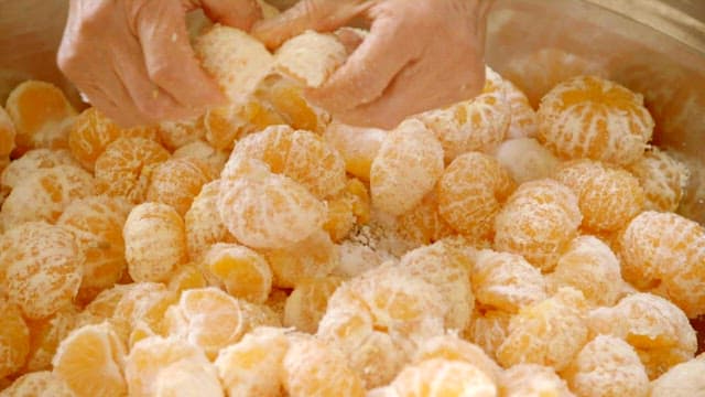 Peeled tangerines, sugar and nuts mixed in a large bowl