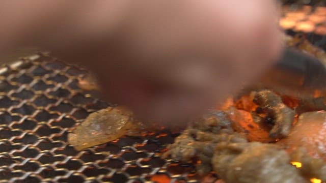 숯불 위 그릴에서 집게로 굽는 먹음직스러운 고기