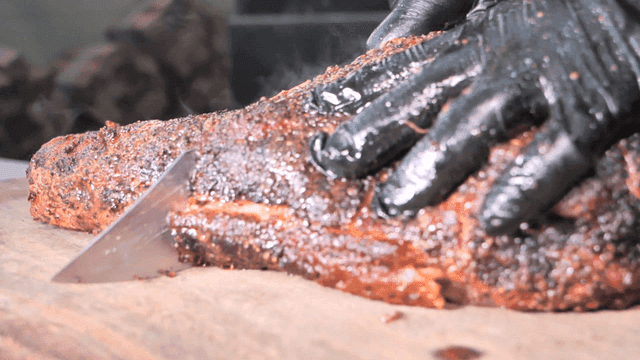 A hand slicing a seasoned brisket