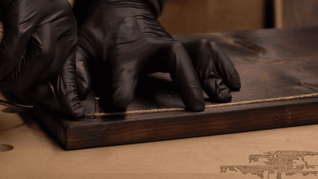 나무 판자 못에 실을 감는 장갑 낀 손