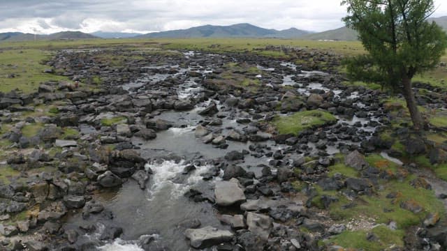 Aerial View of a Stream and Waterfall Flowing Through Grasslands