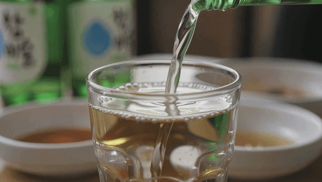 Pouring soju into a glass with dishes