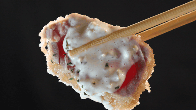 Chopsticks holding tuna topped with sauce