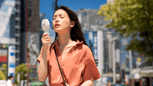 도시에서 손풍기로 더위를 식히는 여성