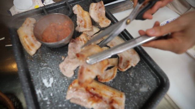 Person cutting sizzling pork belly on a grill