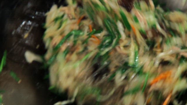 Stir-frying glass noodles, vegetables, and meat in a hot wok