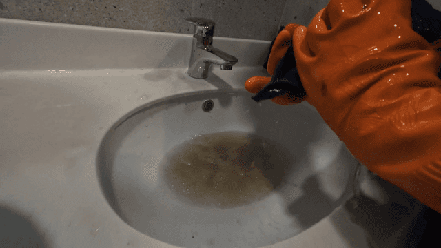 Person wearing rubber gloves wringing out rag that is flushing dirty water into sink