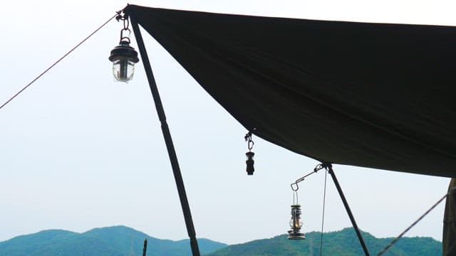 Camping setup with lanterns hanging under a tarp of tent