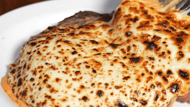Cheese-covered steak on a white plate